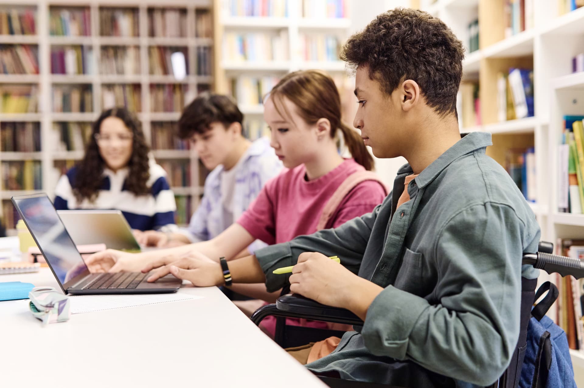 Teenage students studying side by side with laptops in a school library