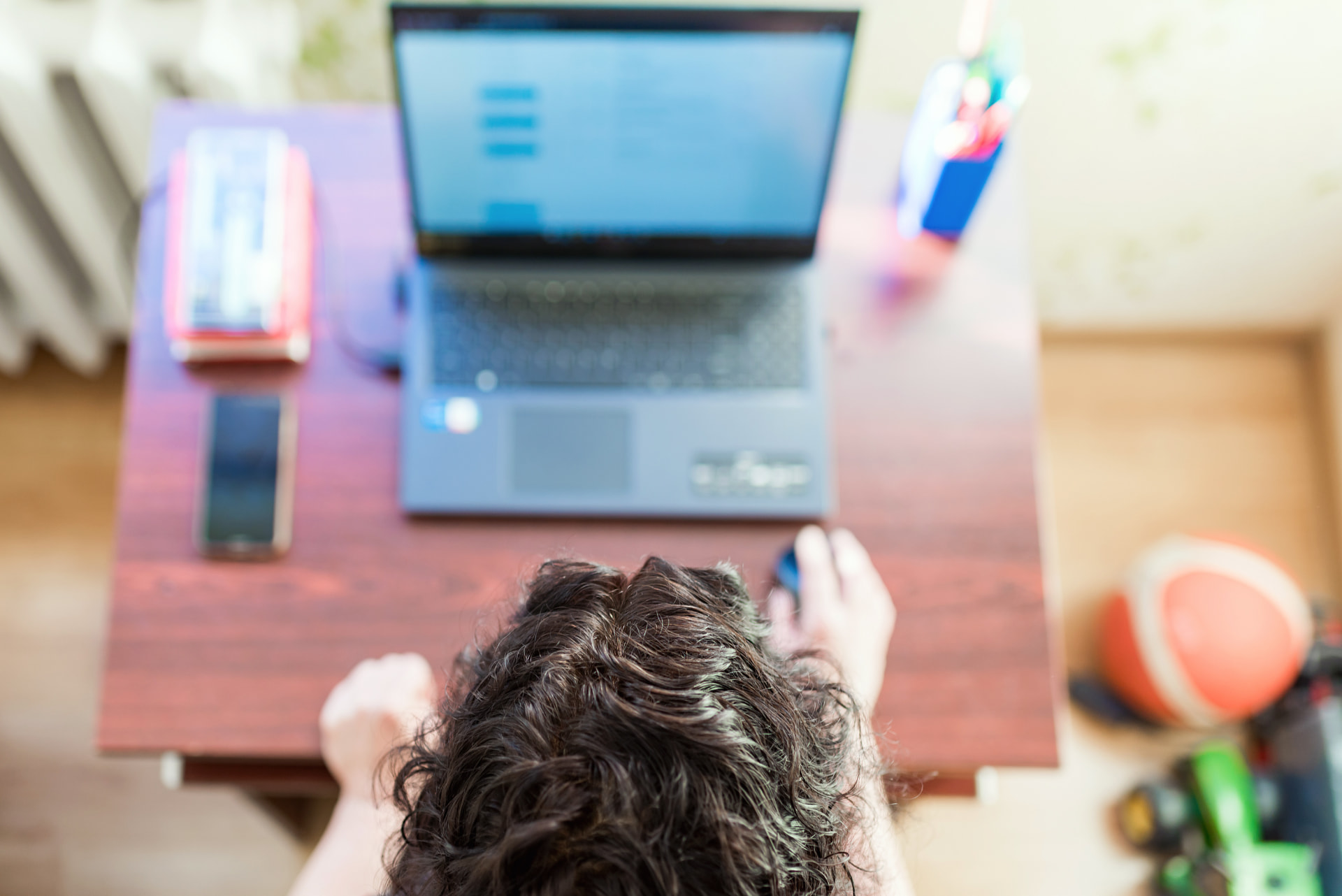 Teenager studying on a laptop on a wooden table, seen from above